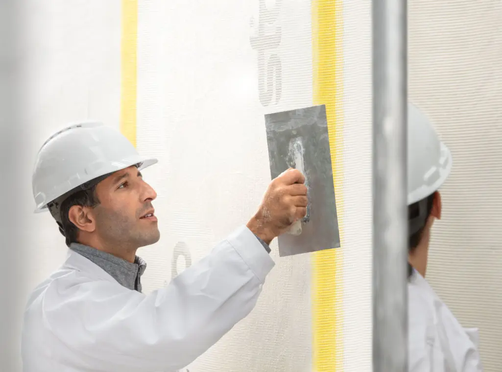 Fachhandwerkerin, Malerin streicht Hausfassade mit einer Walze, Sto-Fassadenfarbe