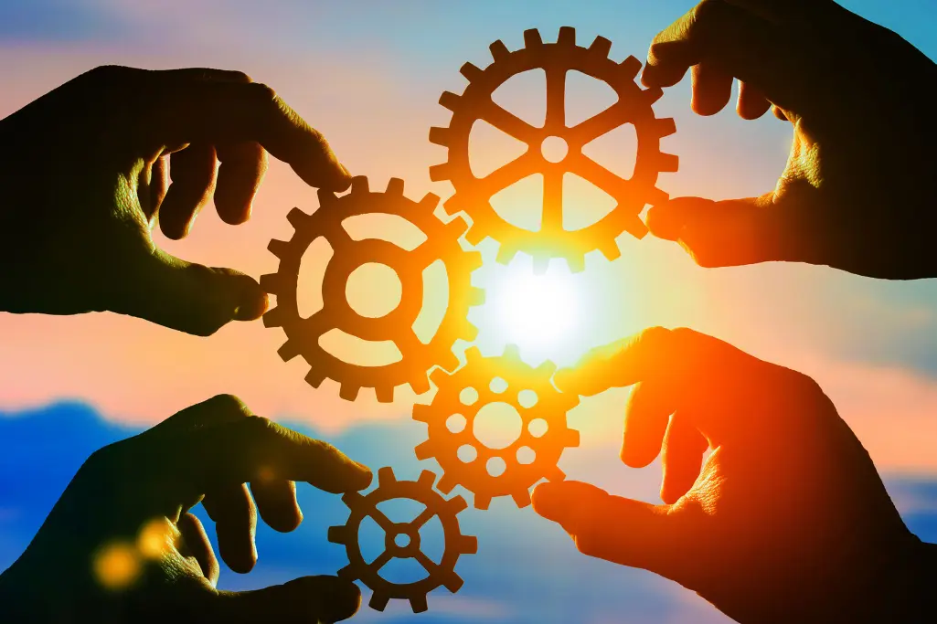 4 Hände halten Zahnräder gegen die Sonne, gut verzahnt, Team, Miteinander