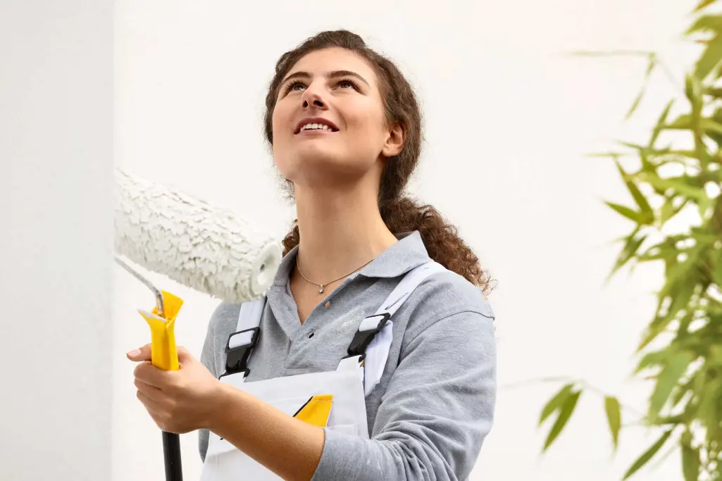 Fachhandwerkerin, Malerin streicht Hausfassade mit einer Walze, Sto-Fassadenfarbe
