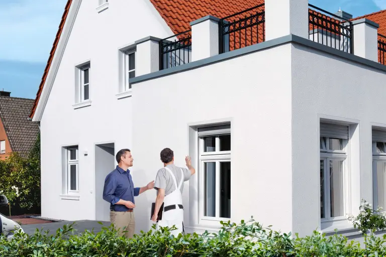 Weißes Einfamilienhaus, davor Hausbesitzer und Fachhandwerker im Gespräch. Dämmen lohnt sich