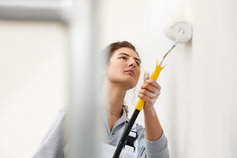 Laboraufnahme, junge Handwerkerin streicht Fassade mit StoColor Lotusan AimS