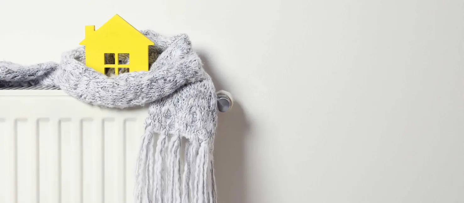 Wärmedämmung Fassade: In einen grauen Schal gewickeltes gelbes Hausmodell steht auf einer Heizung: 