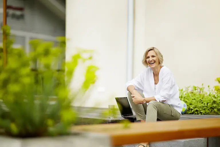 Ökologische Fassadensanierung mit Sto. Lachende Frau sitzt auf der Terrasse vor Ihrem Haus. 