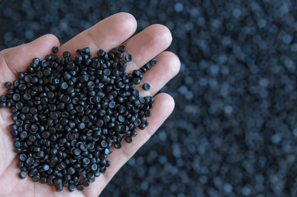 Rohstoff für EPS: Hand hält dunkelgraue Granulatperlen aus Polystyrol