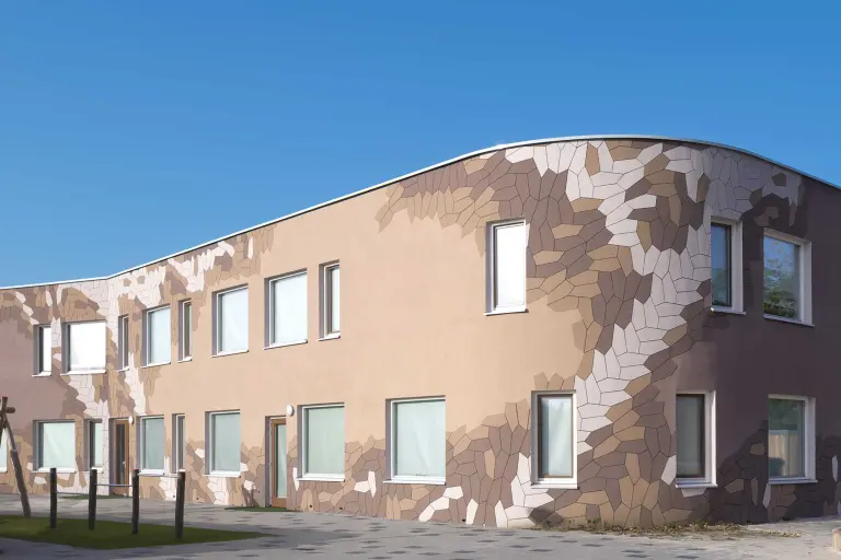 Gedämmte braune Schulfassade mit vorgefertigten Putzelementen StoEcoshapes in Weiß, Beige und Braun