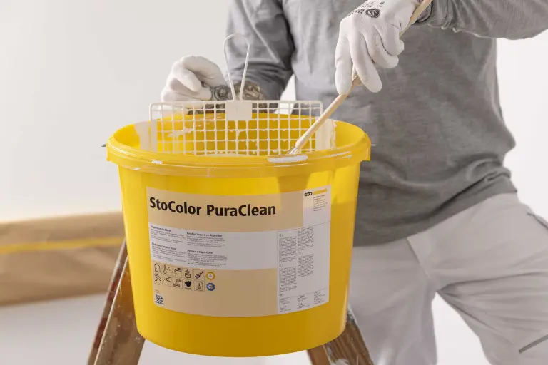 Ein Mann streicht eine Wand, mit der abwaschbaren Wandfarbe StoColor PuraClean. Eimer im Vordergrund
