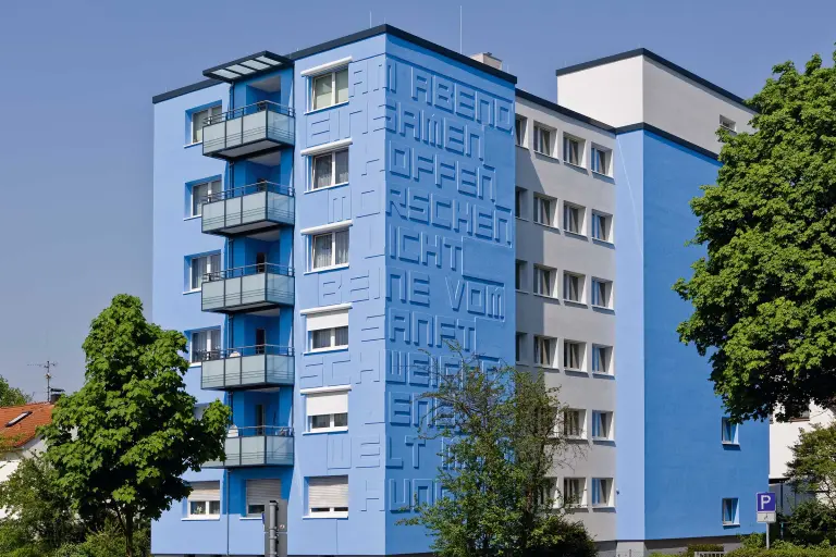 Außenaufnahme eines Mehrfamilienhauses mit blauer Fassade, gestaltet mit StoDeco Buchstaben aus Decoplan-Platten