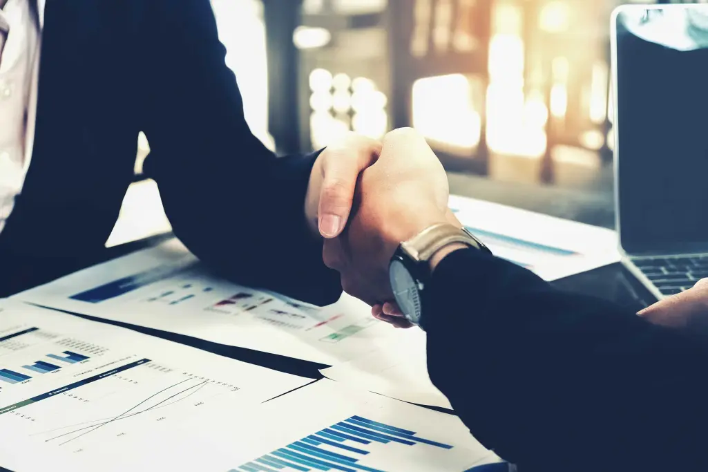 Foto: Handschlag von zwei Geschäftspartnern in schwarzen Anzügen, besiegeln eine Vereinbarung