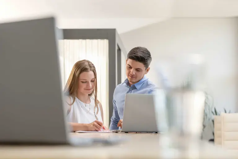 Zwei DH-Studenten von Sto arbeiten gemeinsam vor einem Laptop, Auszubildende links notiert etwas auf einem Block. Foto: Marting Baitinger, Böblingen, DE