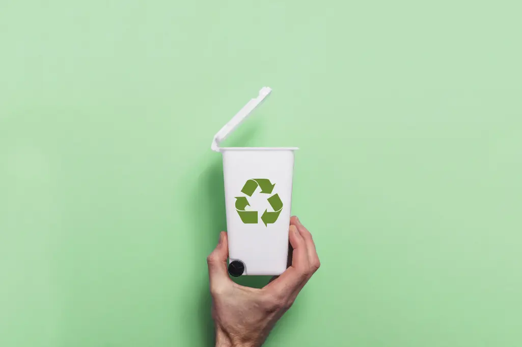 Hand hält weiße Recycling-Mülltonne gegen grünen Hintergrund. Recycling von Steinwolle-Dämmplatten.