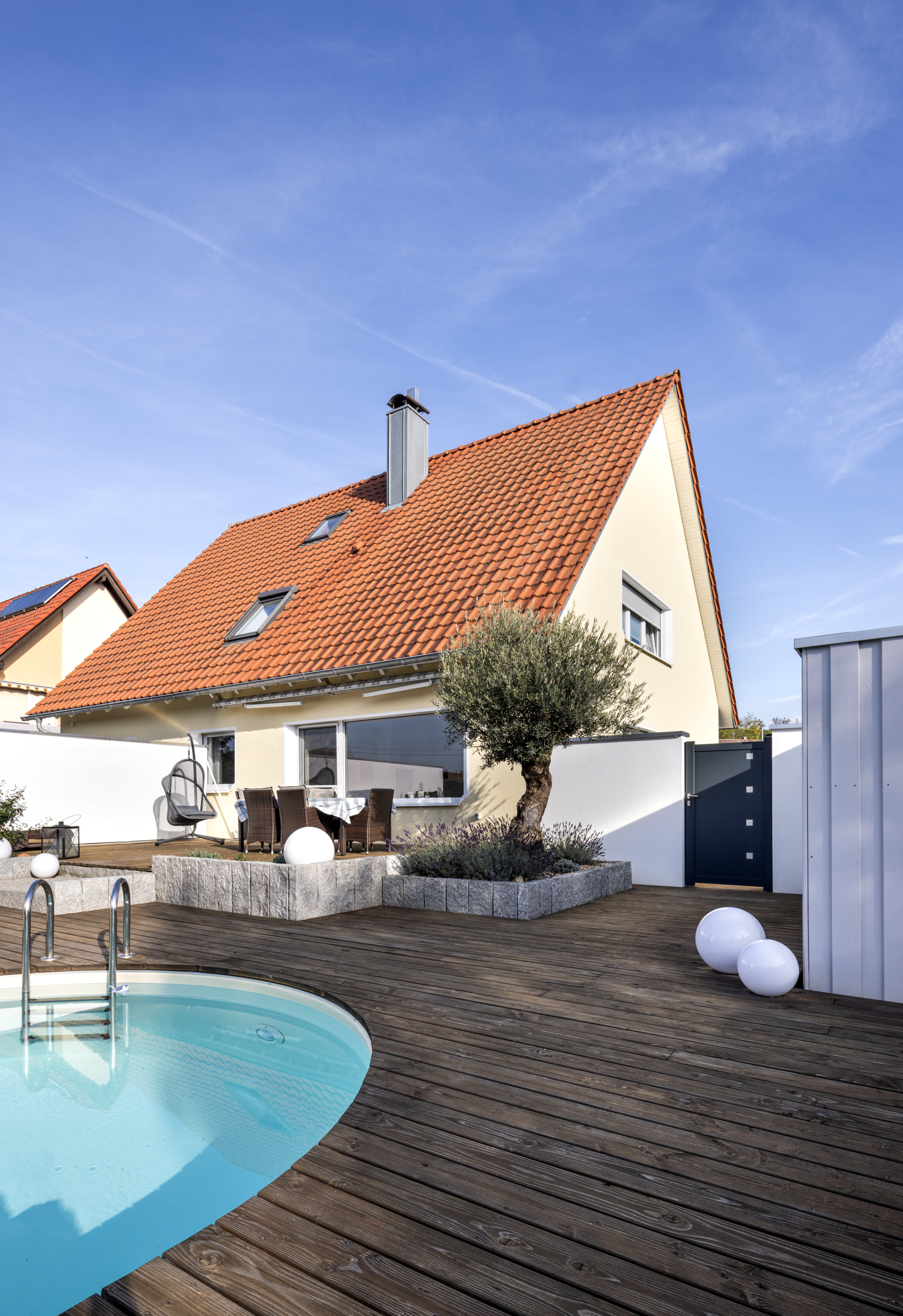 Eine verputzte Wand, teilweise mit Holz verkleidet, bietet im Poolbereich einen Sichtschutz.