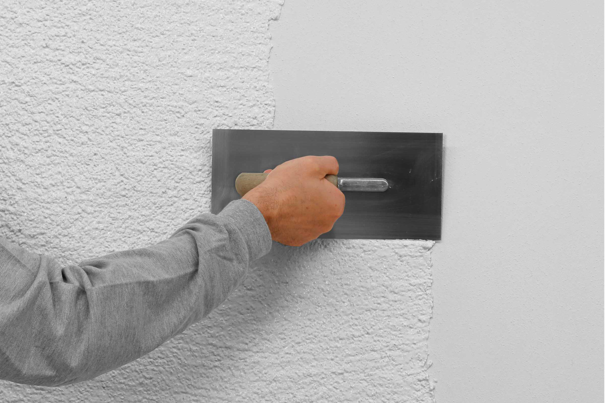 Arm von Handwerker verarbeitet weißen Stolit-Putz mit Kelle an der Wand