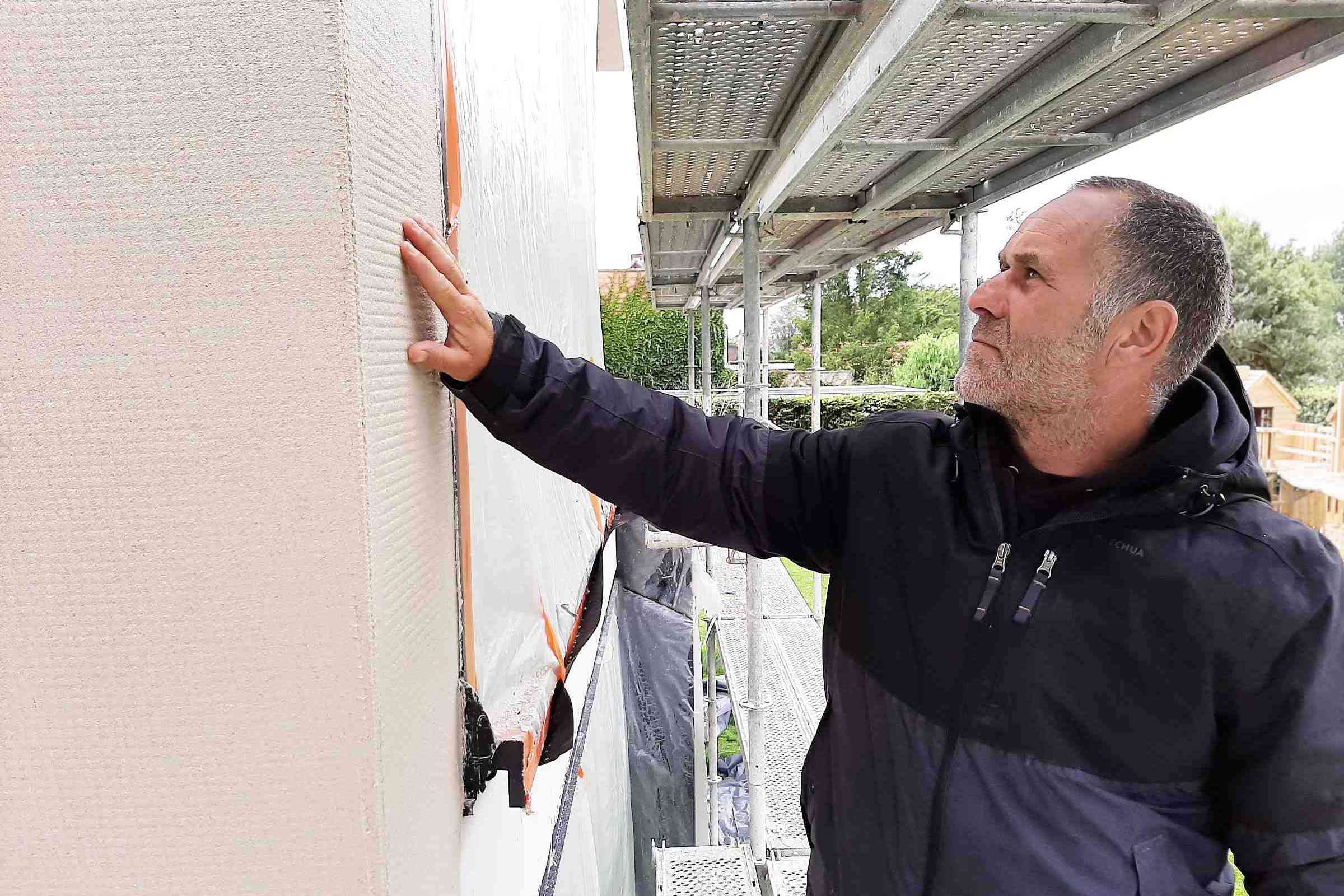Baustelle: Handwerker streicht mit Hand über die Hausfassade