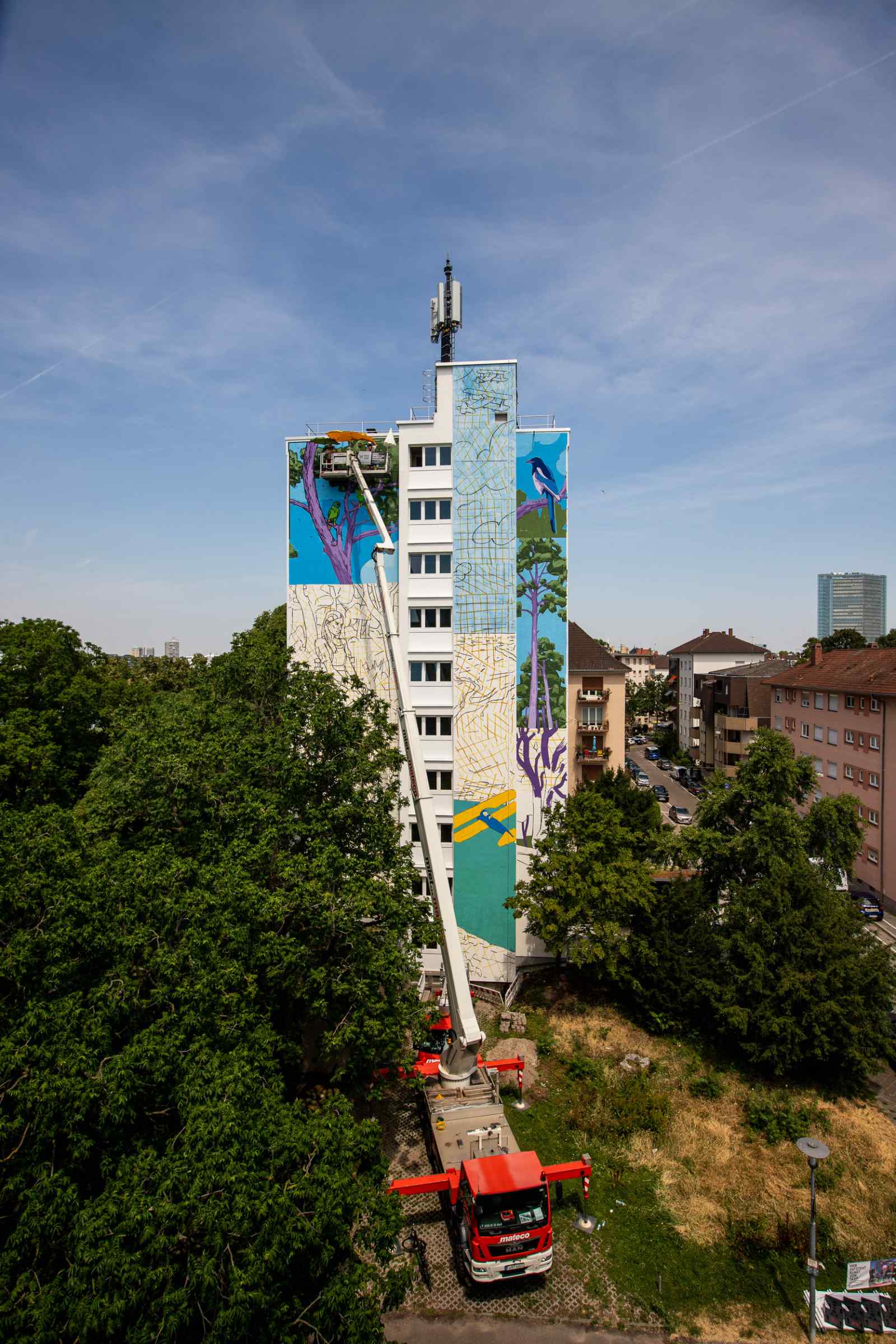 Außenaufnahme von Malerarbeiten an der Hochhaus-Fassade mit Hebebühne. Das Mural „In Contemplation"