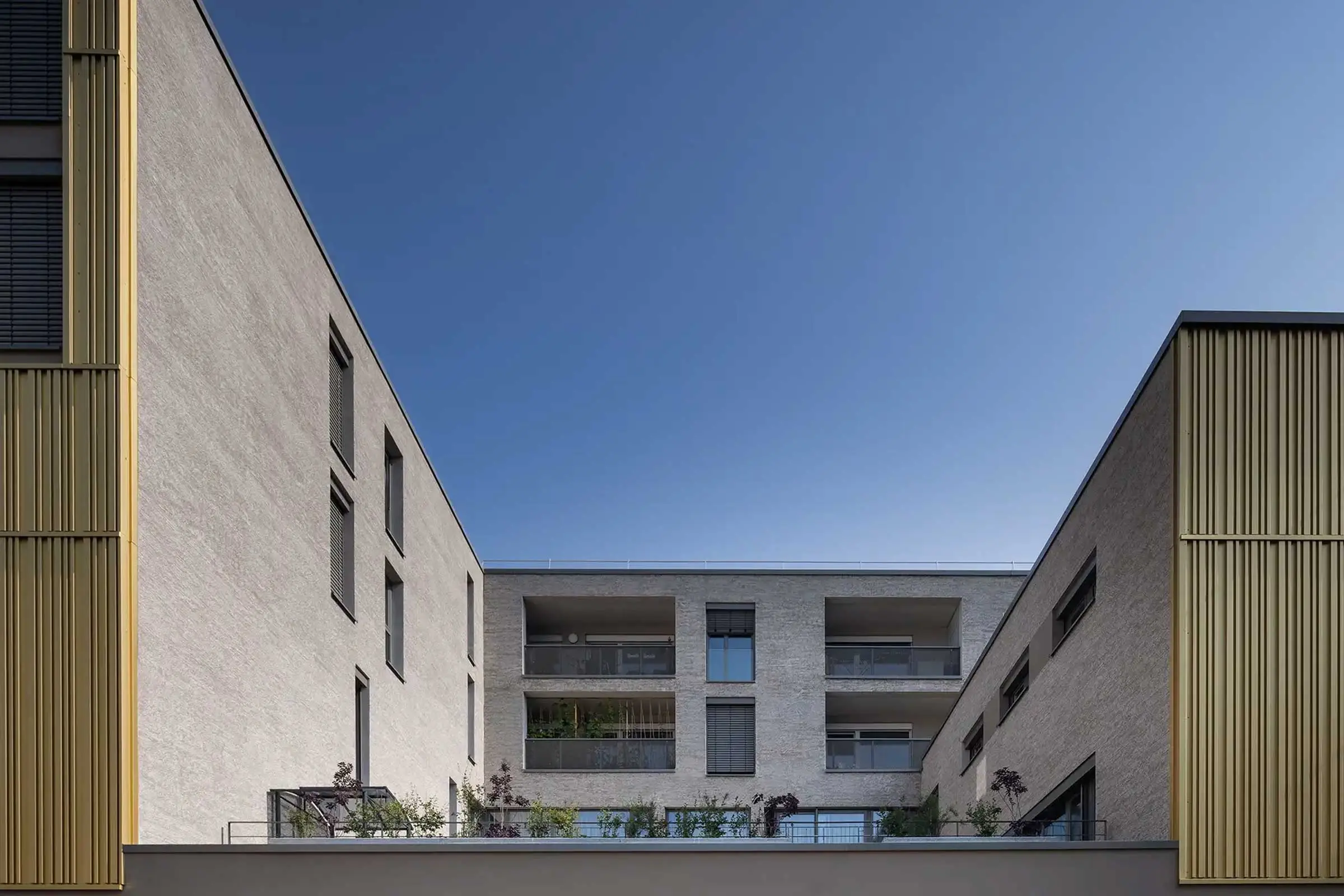 Wohn- und Geschäftsgebäude in Erdtönen mit Sto-Wärmedämmung und goldenen Architekturelementen