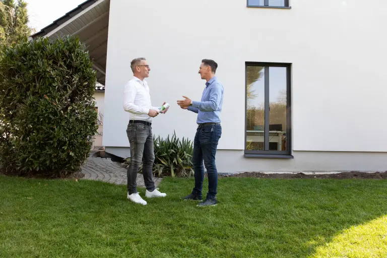 Zwei Männer unterhalten sich vor einem Haus im Garten