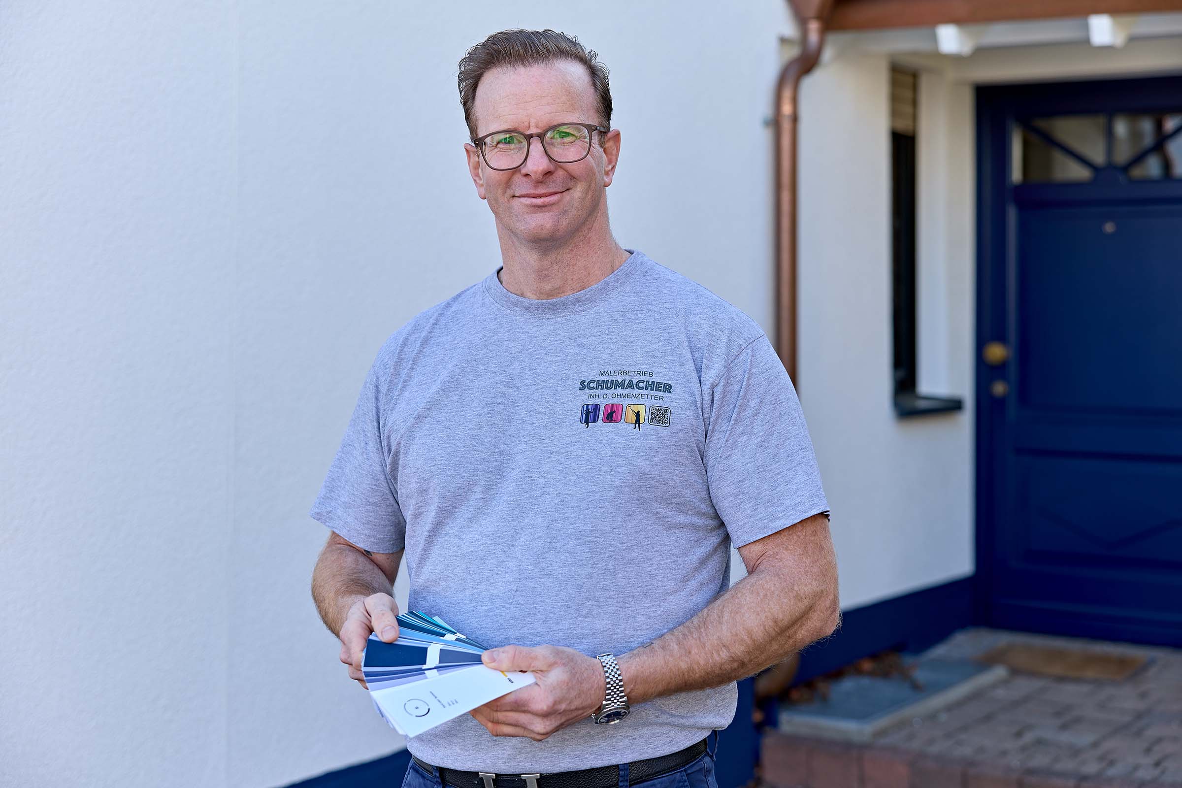 Ein Mann hat einen Farbtonfächer in der Hand und steht vor einem Einfamilienhaus